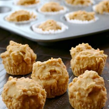 five mini carrot cake muffins on a wood table with a muffin tin in the background