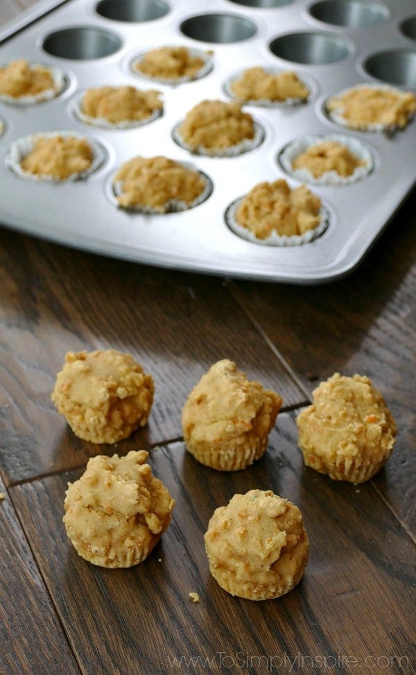 five mini carrot cake muffins on a wood table with a muffin tin in the background