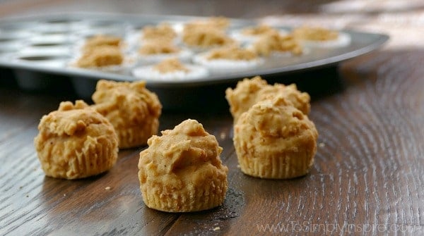 four mini carrot cake muffins on a wood table with a muffin tin in the background