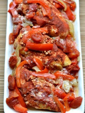 A closeup of Chicken with sliced red bell peppers and paprika on a white plate