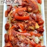 A white plate of Chicken with sliced red bell peppers and paprika