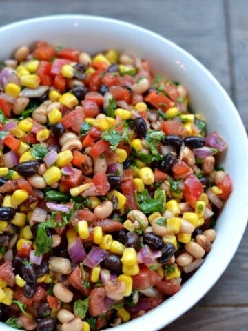 closeup of Cowboy Caviar recipe with corn black beans, tomatoes and cilantro in a white bowl