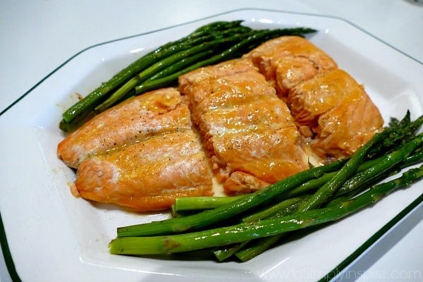 a closeup of a white plate with 3 salmon slices and asparagus on the side