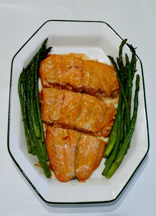 a white plate with 3 salmon slices and asparagus on the side