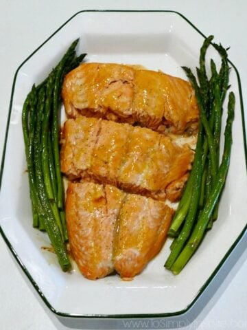 a white plate with 3 salmon slices and asparagus on the side