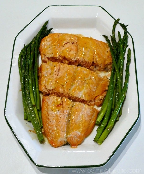 a white plate with 3 salmon slices and asparagus on the side