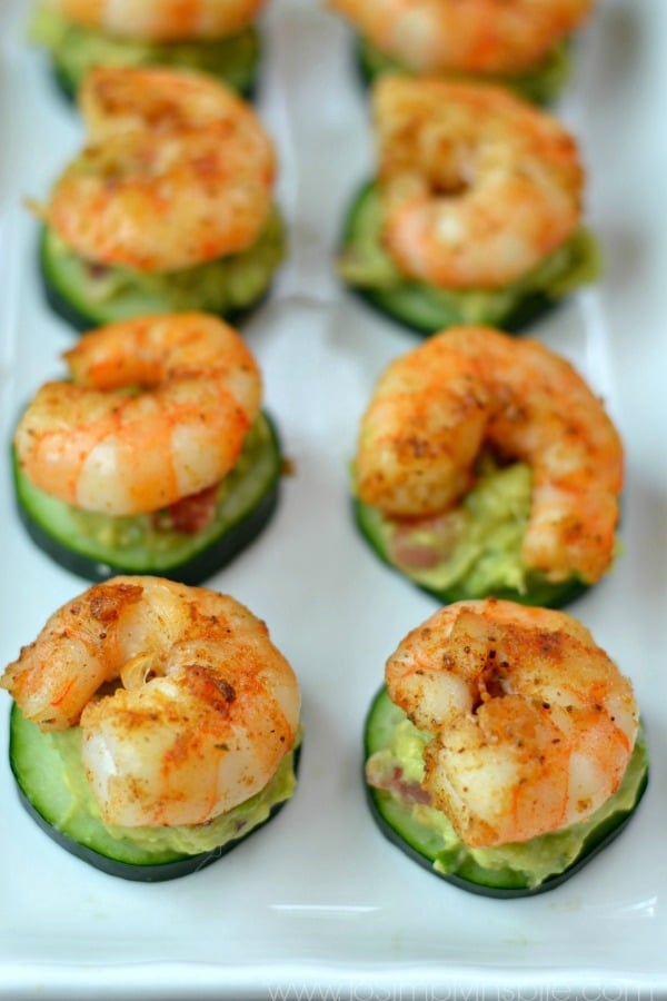 an appetizer of a group of 6 shrimp sitting on cucumber slices and avocado