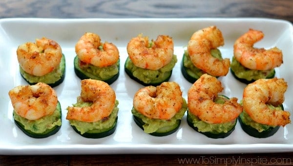 A tray of food on a plate, with Shrimp on top of cucumber slices and avocado