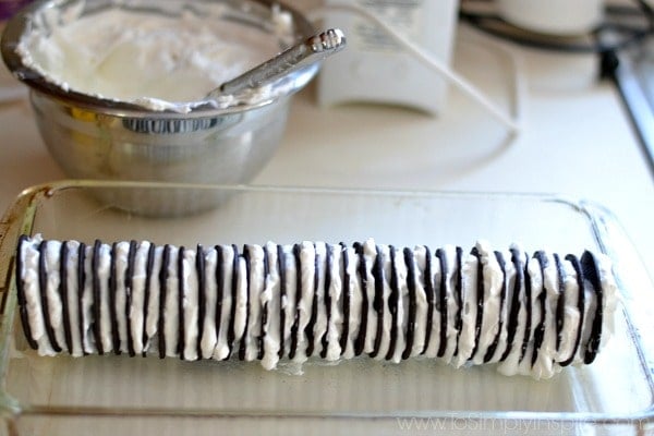 Famous Chocolate Wafer Cake layers in a glass dish with a bowl of whipped cream in the background