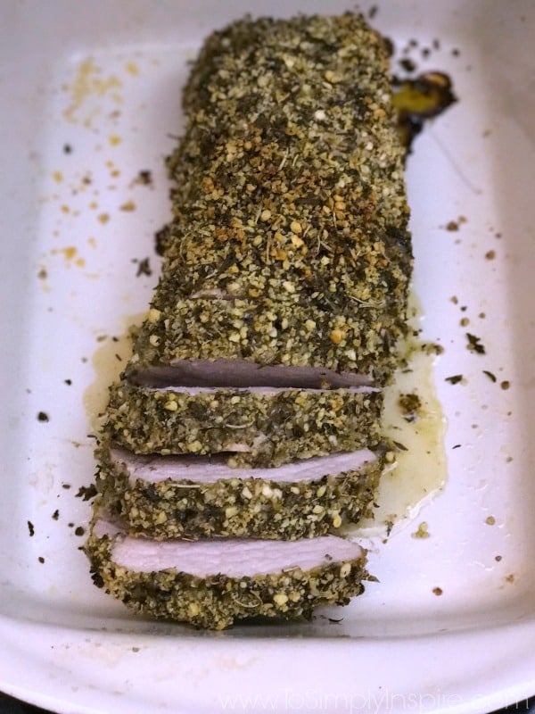 Herb Crusted Pork Tenderloin topped with bread crumbs and herbs on a white plate
