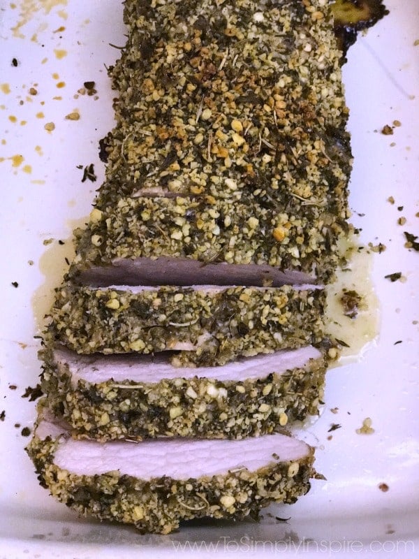 a plate with sliced Herb Crusted Pork Tenderloin topped with bread crumbs and herbs