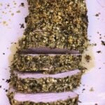 a plate with sliced Herb Crusted Pork Tenderloin topped with bread crumbs and herbs