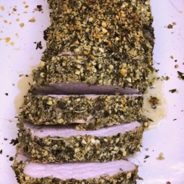 a plate with sliced Herb Crusted Pork Tenderloin topped with bread crumbs and herbs