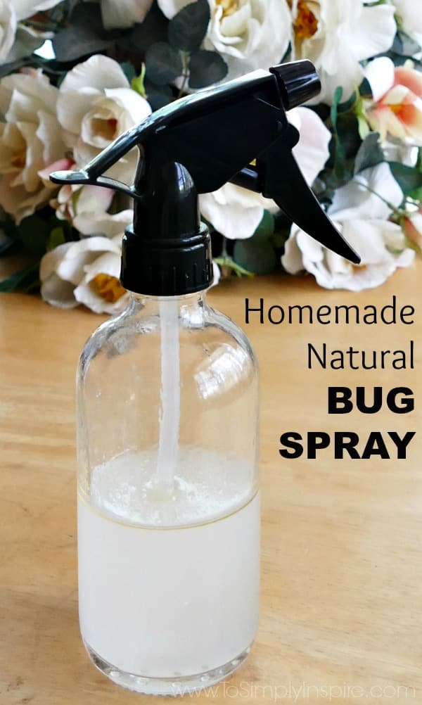 Glass Spray bottle with black top half filled with liquid homemade bug spray with flowers in the background