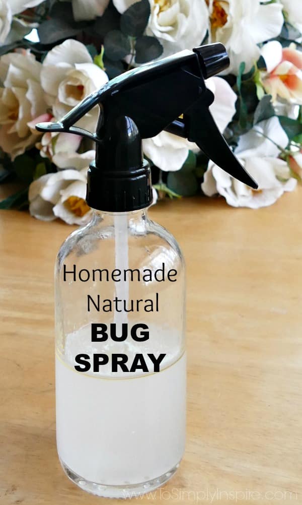 Glass Spray bottle with black top half filled with liquid homemade bug spray with flowers in the background