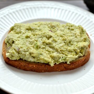 A white plate with a piece of bread on a plate with Avocado Chicken salad on top