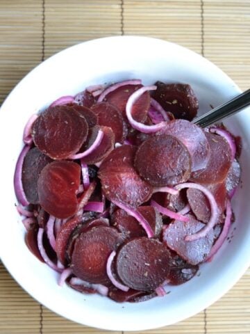 A white bowl with sliced beets and red onion with a spoon