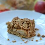 Apple Oatmeal Crumb Bar on a white plate with an apple and dish in the background.