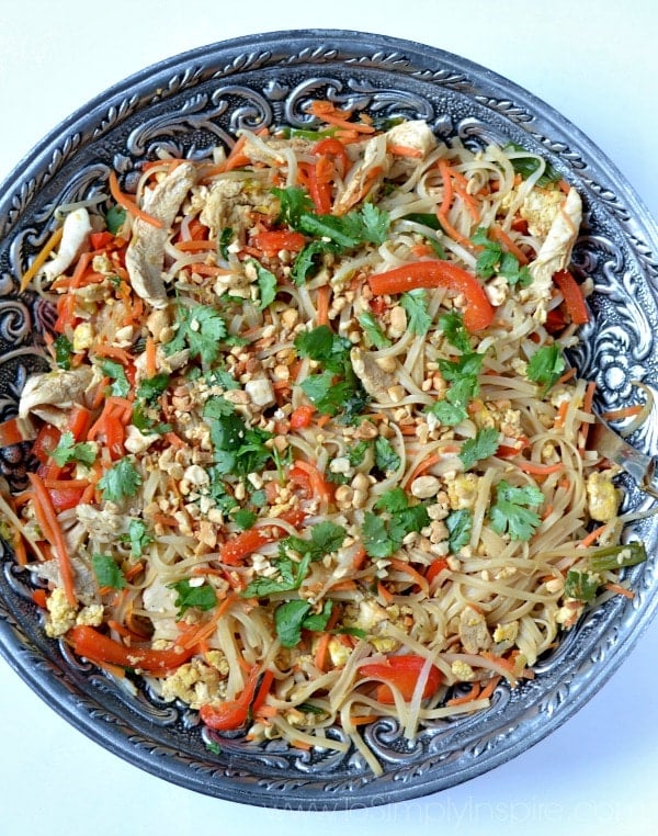 A big silver bowl rice noodles, red pepper strips, cilantro, chicken and peanuts