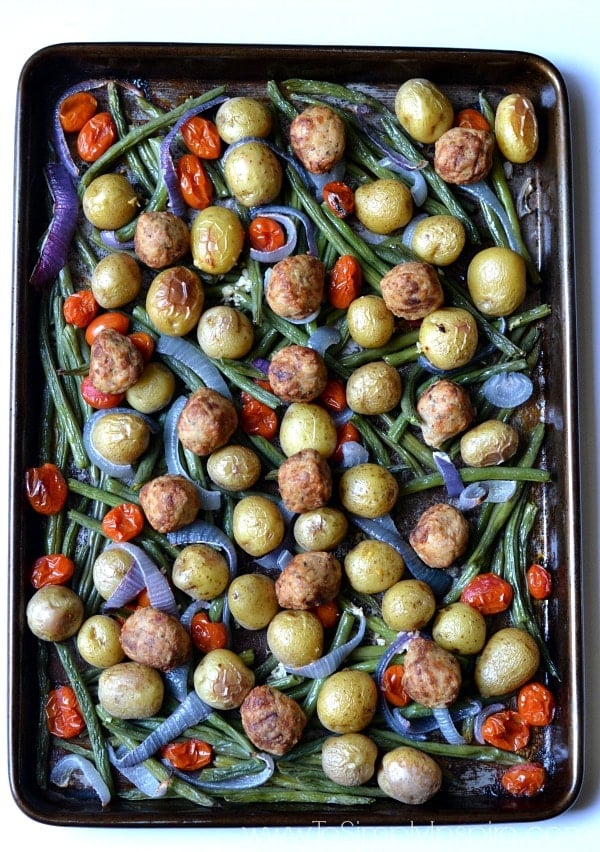 Meatballs with roasted potatoes, green beans and red peppers on a baking sheet.