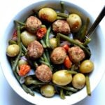 Meatballs with roasted potatoes, green beans and red peppers in a white bowl.