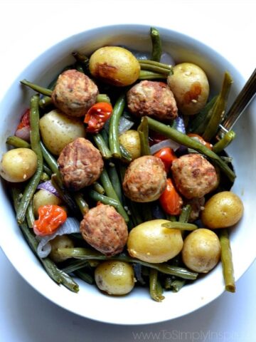 Meatballs with roasted potatoes, green beans and red peppers in a white bowl.