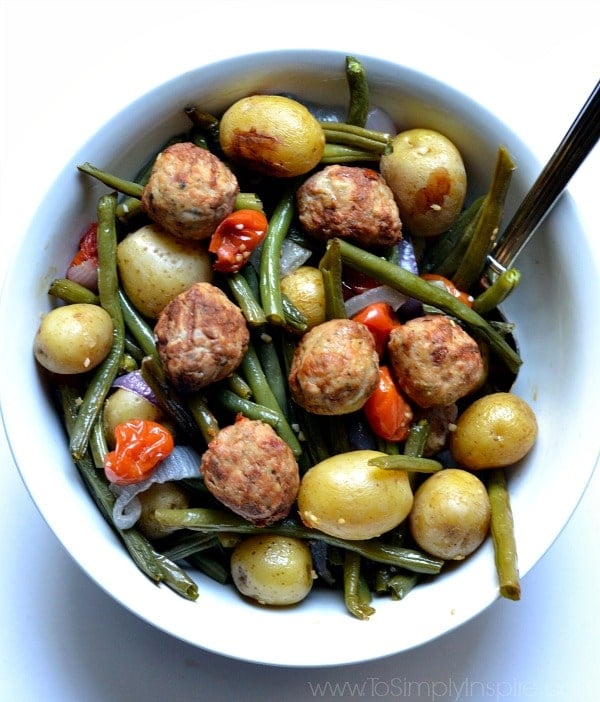 Meatballs with roasted potatoes, green beans and red peppers in a white bowl.