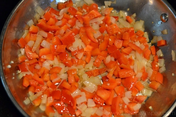 Diced red bell peppers and onions cooking in a stainless steel pan