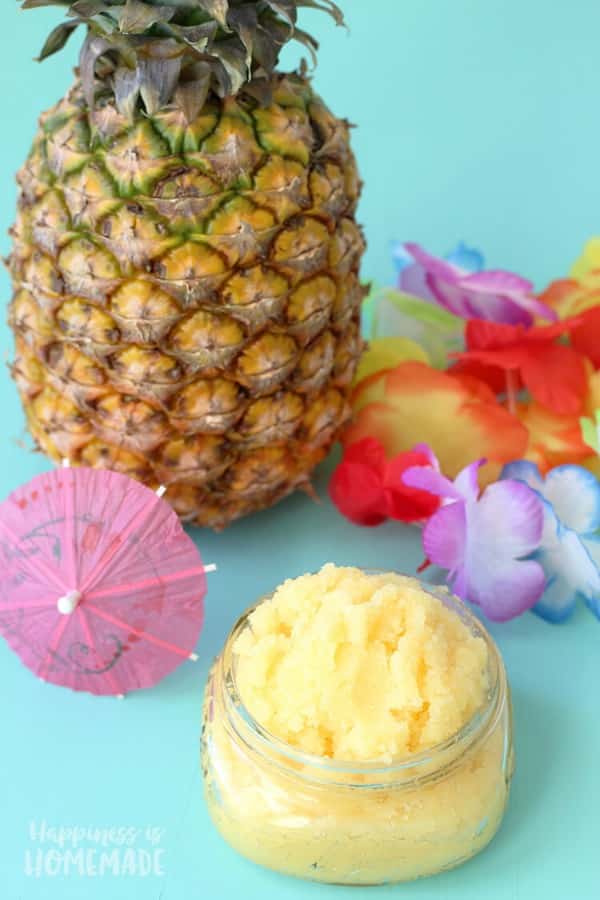 yellow sugar scrub in a glass dish with a pineapple and hawaiian flowers behind