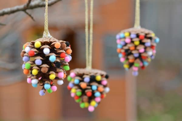 a closeup of a DIY pom pom pinecone Christmas ornament hanging on a tree