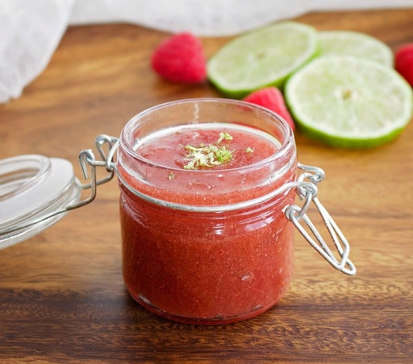 raspberry lime sugar scrub with slices of lime and raspberries behind.