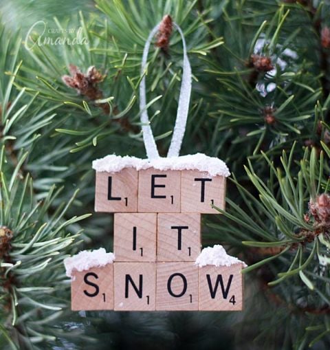 a closeup of a DIY scrabble tile Christmas ornament that says Let it Snow hanging on a tree