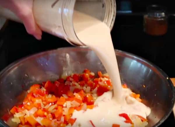 white sauce pouring over diced red peppers and onions
