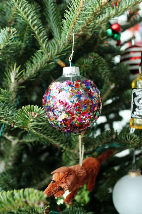 a closeup of a Christmas ornament filled with colorful confetti hanging on a tree