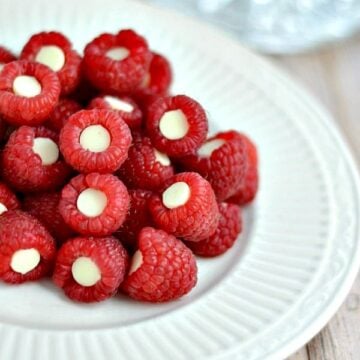 A close up of raspberries with white chocolate chip inside each on a white plate