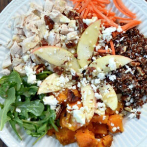 a white bowl fulll of chicken, quinoa, sweet potato, arugula and apple