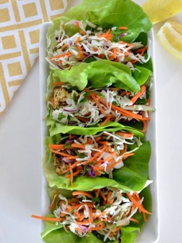 a rectangle plate with Lemon Herb Chicken Lettuce Wraps topped with Citrus Slaw
