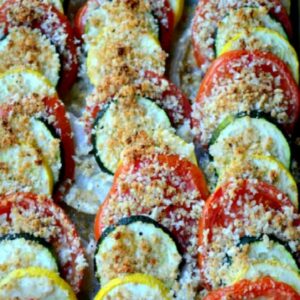 zucchini , yellow squash and tomatoes layered in a dish.