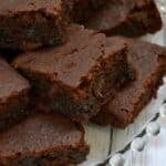 A close-up of several rich, fudgy gluten-free brownies stacked on a glass plate.