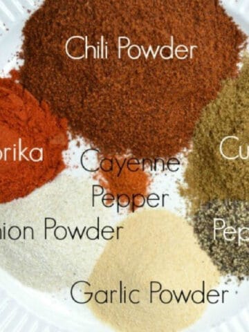 several seasonings in piles on a plate labeled with their names. Chili powder, paprika, cumin, onion powder, garlic powder, pepper and cayenne