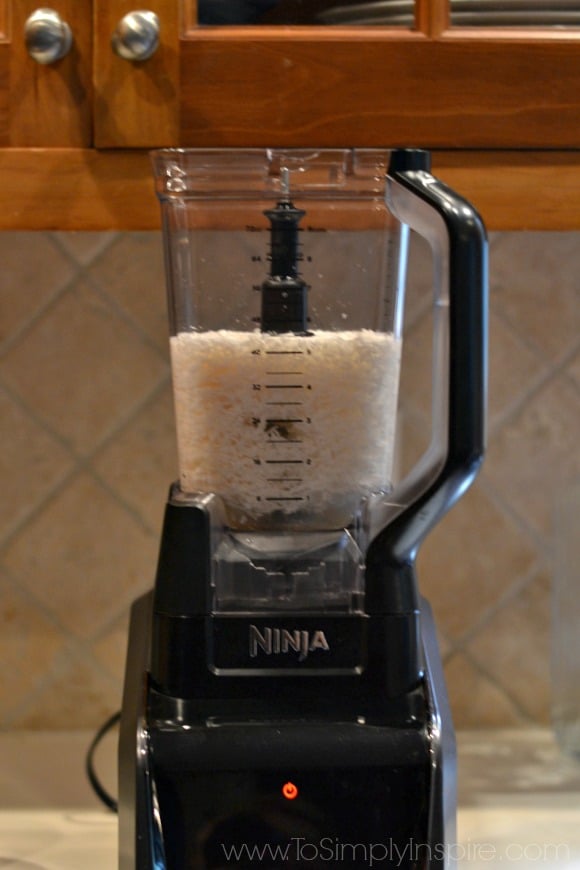 A blender sitting on a counter with shredded coconut and water