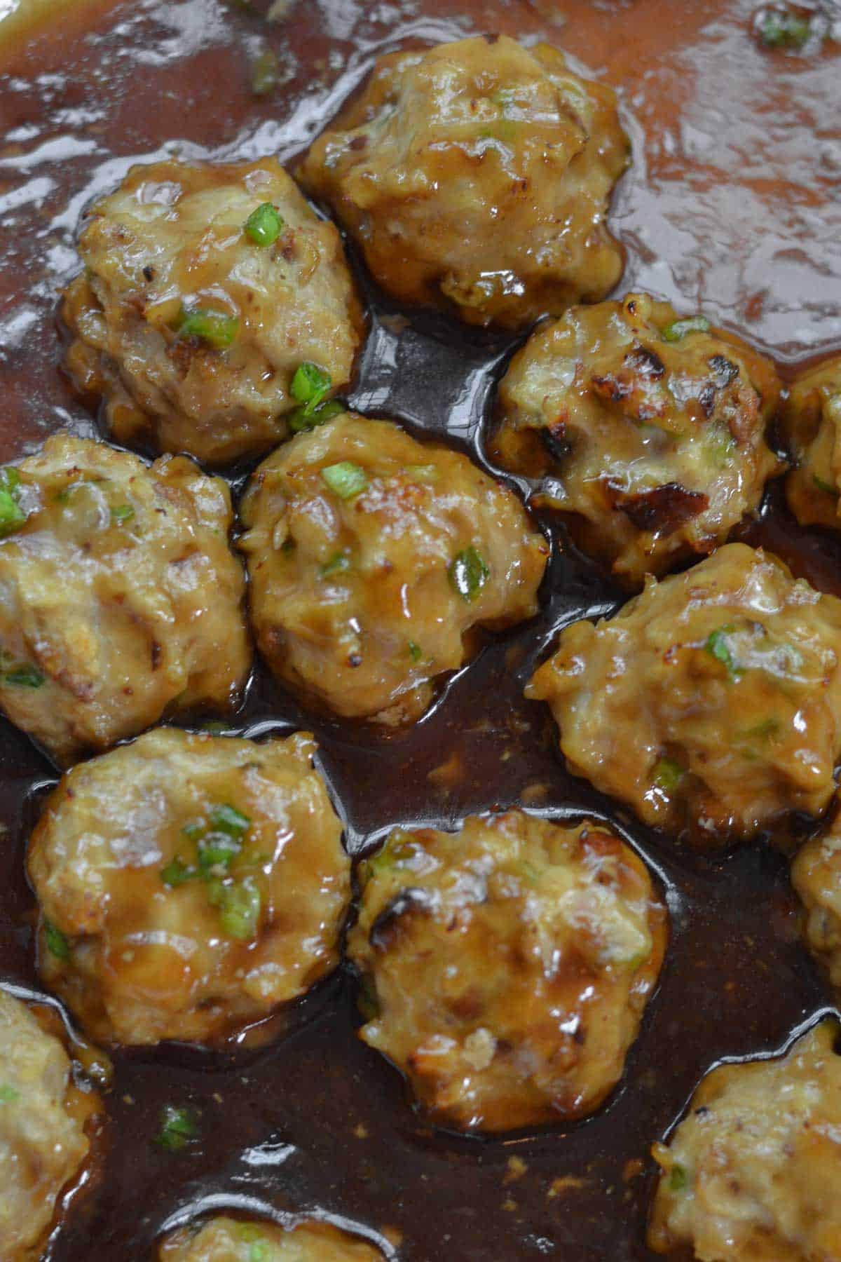 Teriyaki Chicken Meatballs are healthy, delicious and perfectly seasoned in a savory sauce. So easy to make with simple all natural ingredients. Closeup of a panful Teriyaki Chicken Meatballs Recipe in a brown sauce.