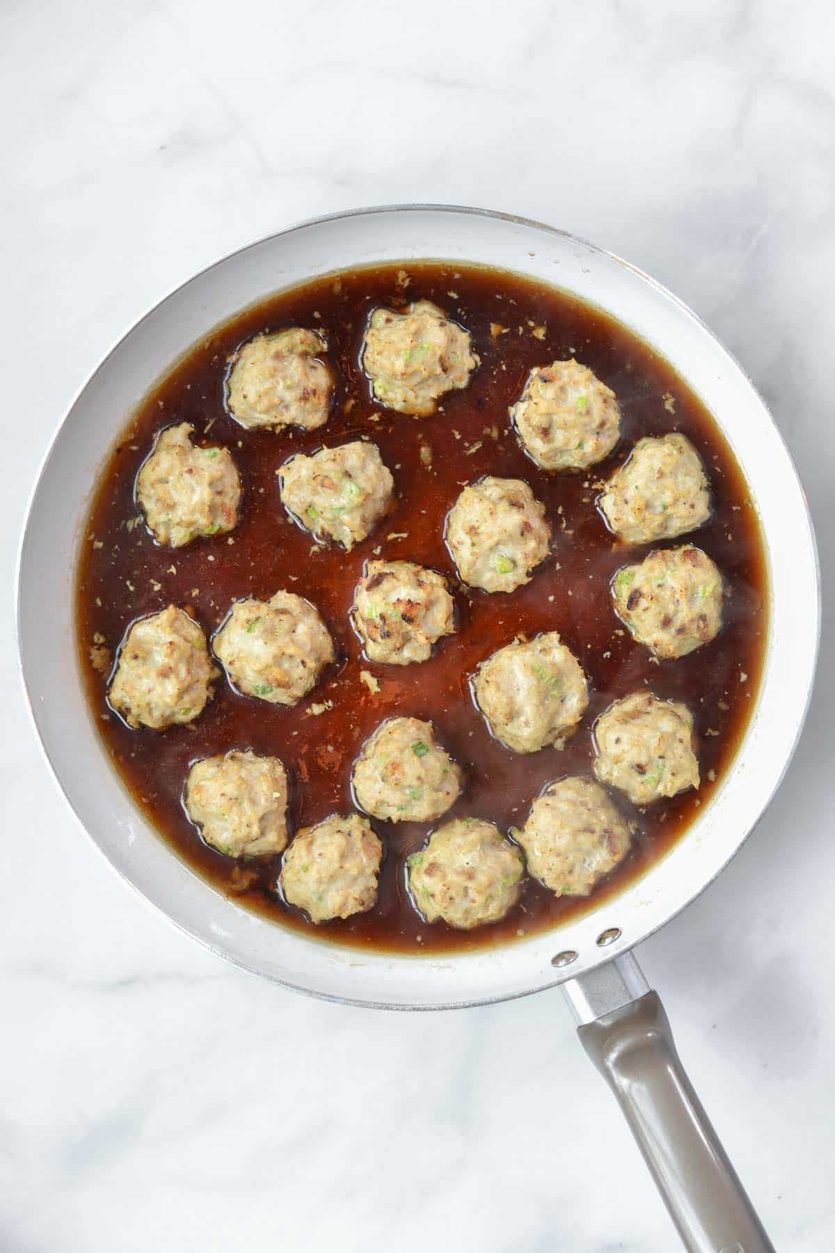 Closeup of seventeen Teriyaki Chicken Meatballs in a saute pan. 