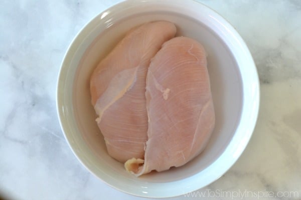 A white bowl with 2 uncooked Chicken breasts soaking in water