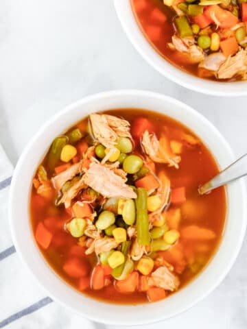 chicken vegetable soup with corn and green beans in a white bowl with a spoon