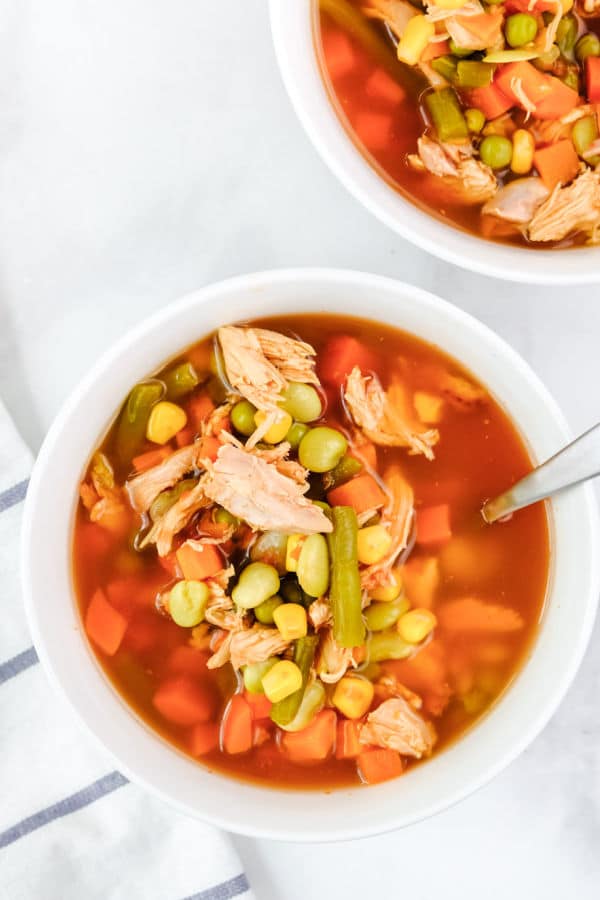 chicken vegetable soup with corn and green beans in a white bowl with a spoon