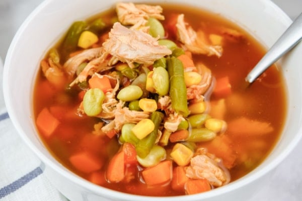 closeup of chicken soup with corn, tomatoes, green peas and green beans