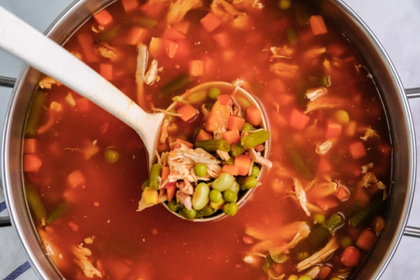 overhead of a ladle full of chicken vegetable soup over a big pot of soup