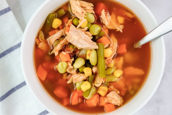 closeup of chicken vegetable soup in a white bowl with a spoon