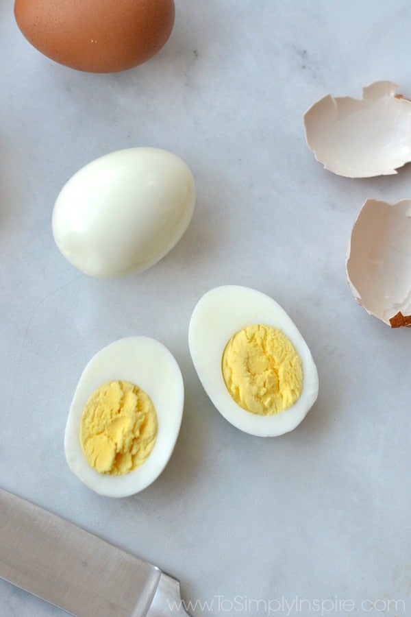 Hard boiled egg cut in half with yolks showing surrounded by shell and another peel egg